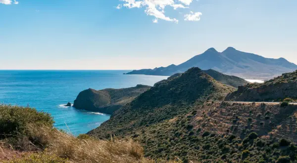 Paisaje costero en Cabo de Gata, con el mar azul intenso y montañas verdes.