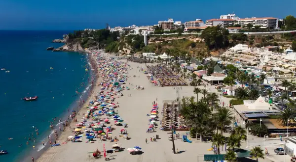Vista aérea de la bulliciosa playa de Burriana, considerada la mejor playa de Nerja, con gente disfrutando del sol y el mar azul.