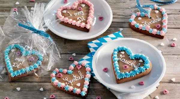 Bunte Lebkuchenherzen selber machen: mit Zuckerguss und Sprüchen verziert, liegen sie auf Holztisch.