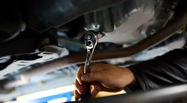 Dłoń mechanika dokręca kluczem nasadowym korek spustowy oleju. Ważne jest, z jaką siłą dokręcać korek spustowy oleju, by nie uszkodzić miski olejowej.