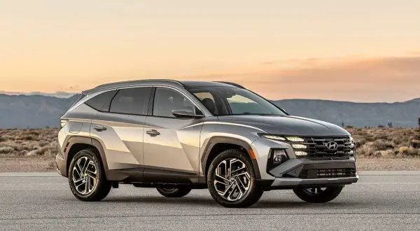 Silver Hyundai Tucson Hybrid testbil parkerad på en väg med berg i bakgrunden.