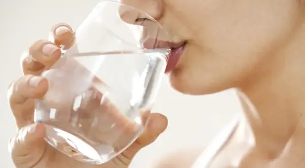 Une femme boit un verre d'eau. Une question importante pour les jeunes mamans : quelle eau boire allaitement ?