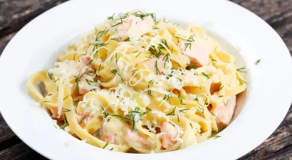 Pyszne fettuccine z łososiem w kremowym sosie, posypane parmezanem i świeżym koperkiem. Idealne danie dla miłośników ryb.