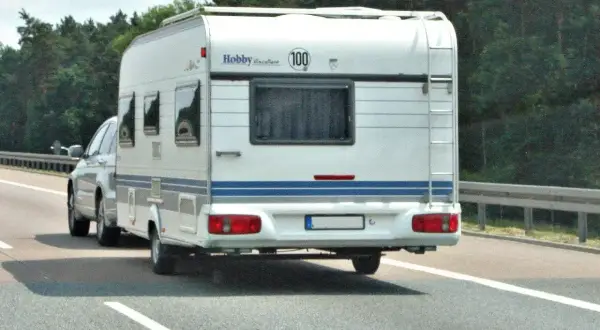 Biała przyczepa kempingowa Hobby jedzie autostradą. Kierowca z kod 96 prawo jazdy wiezie rodzinę na wakacje.