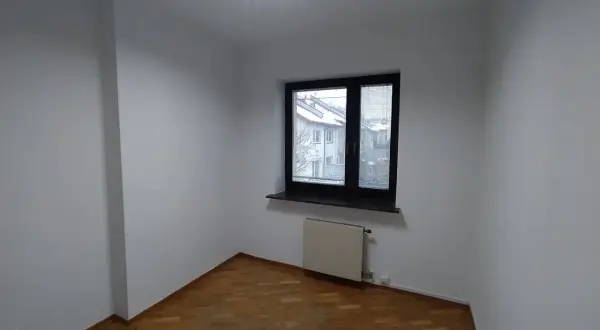 Puste, białe pomieszczenie z drewnianą podłogą i oknem. Zastanawiasz się, ile trwa malowanie pokoju?