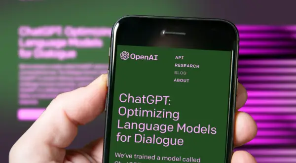 Dłoń trzyma smartfon z otwartą stroną OpenAI, prezentującą ChatGPT: Optymalizację modeli językowych do dialogu.