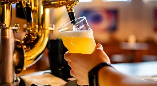 Hand holding a glass of beer being poured from a golden beer tap.