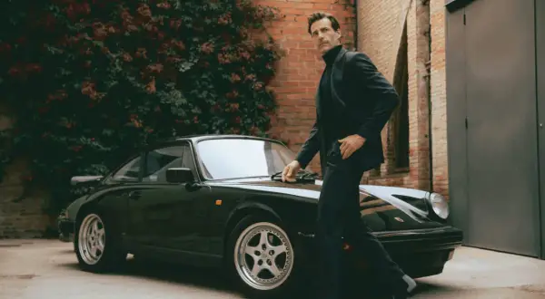 Mann im Anzug und Chelsea Boots lehnt an einem Porsche.