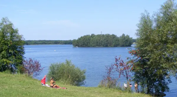 Słoneczny dzień nad jeziorem Chechło-Nakło. Kobieta odpoczywa na trawie, w tle błękitna woda i zielone wyspy.