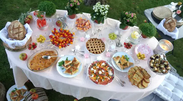 Un magnifique buffet pour une idée pique-nique : tartes, brochettes de fruits, salades, pain et boissons rafraîchissantes sur une table dressée en extérieur.