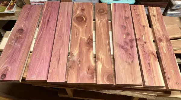 Tablones de madera de enebro con vetas rosadas y nudos visibles, apilados sobre un palé.