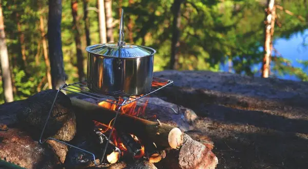 Olla de metal sobre una parrilla encima de una fogata, lista para cocinar. Un bushcrafter prepara su comida en la naturaleza.