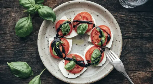 Tomate-Mozzarella-Salat mit frischem Basilikum und Balsamico-Glasur auf einem rustikalen Teller.