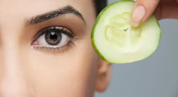 Une tranche de concombre est tenue près de l'œil, une méthode naturelle pour enlever les poches sous les yeux.