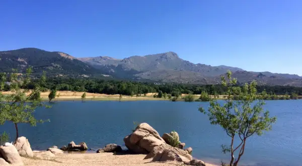 Tranquilo embalse de Navacerrada con montañas al fondo y rocas en la orilla.