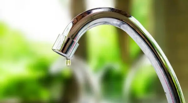 Close-up of a dripping chrome faucet with a water droplet forming.