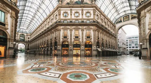 Ett tomt, lyxigt modehus i Milano med en vacker mosaikgolv och glastak. Louis Vuitton-butiken lyser upp.