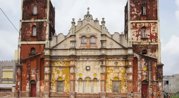 Façade d'une église à Porto-Novo, aux tours jumelles imposantes et à la peinture écaillée, avec des enfants jouant devant.