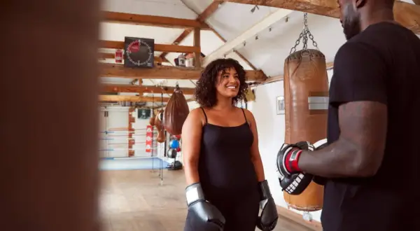 A woman in boxing gloves smiles at a trainer in a gym. This scene suggests that boxing makes you stronger, both physically and mentally.