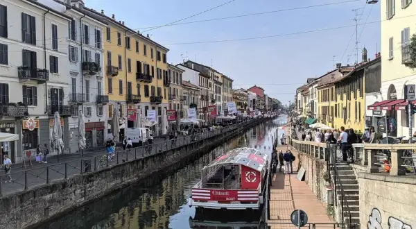 En båt på Navigli i Milano, omgiven av färgglada byggnader och folk som promenerar längs kanalen.