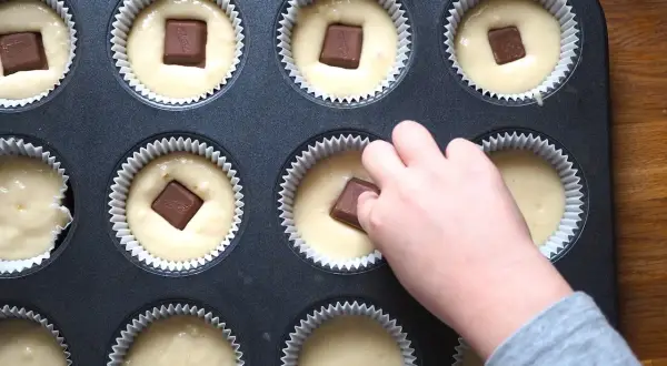 Dziecko wkłada kostkę czekolady do ciasta na muffinki. Prosty sposób, jak udekorować muffinki, by były pyszne.