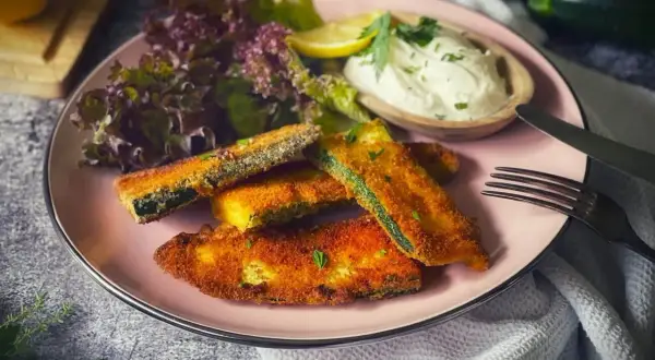 Knusprig panierte Zucchini-Sticks mit Dip, Salat und Zitrone. Ein leckerer Snack für zwischendurch.