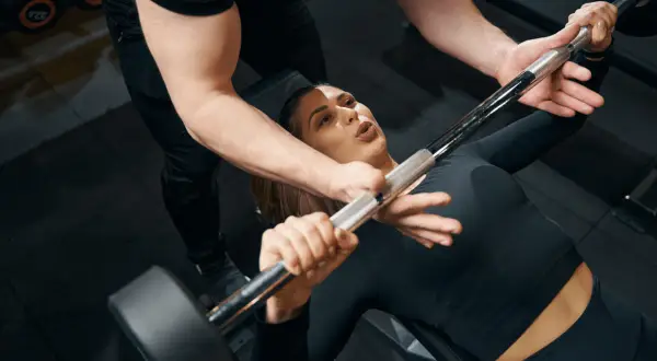 Une femme commence la musculation avec un haltère, guidée par un coach.