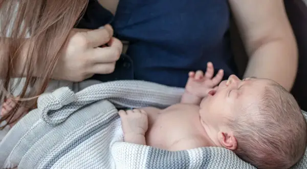 En bebis frustrerad vid amning, med öppen mun och knutna händer, insvept i en stickad filt.