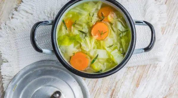 Une marmite de soupe au chou, avec des carottes et des herbes, sur une serviette blanche.