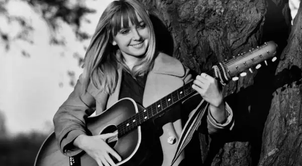 Maryla Rodowicz z gitarą, jakby śpiewała "Wielka woda", oparta o drzewo.