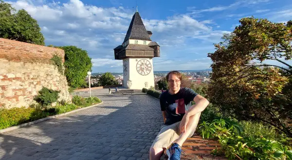 Mann sitzt vor dem Uhrturm in Graz. Ein toller Ort für graz geheimtipps mit Blick über die Stadt.