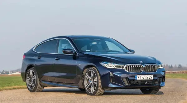 Eleganckie, granatowe BMW 640i na tle pól i błękitnego nieba.