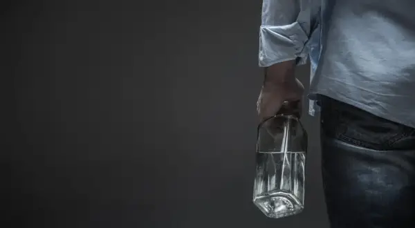 Mężczyzna trzyma butelkę z płynem, sugerującą potencjalną dawkę śmiertelną alkoholu.