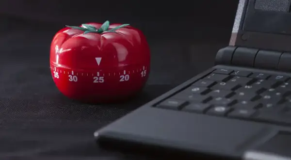 Czerwony minutnik w kształcie pomidora obok klawiatury laptopa, gotowy do pracy metodą pomodoro.