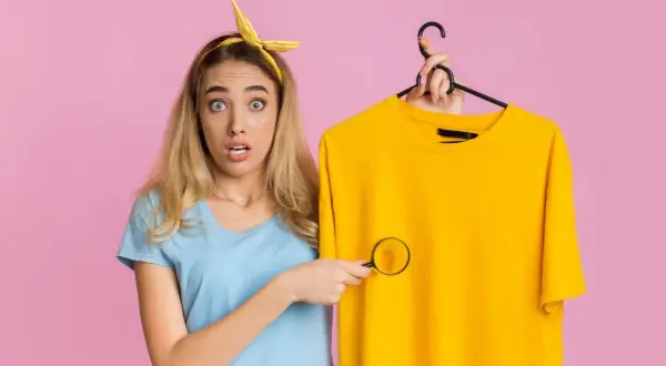 Ragazza sorpresa scopre macchie di detersivo sui vestiti con una lente d'ingrandimento.