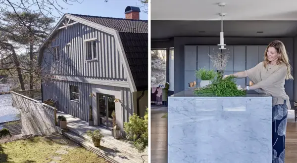 Ett grått egnahemshus från 40-talet med träfasad och altan vid vattnet. I köket arrangerar en kvinna grönska på en marmorö.