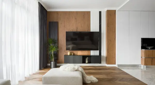 Un salon moderne avec un sol en parquet en chevrons, un mur texturé en bois et un meuble TV suspendu. Un mélange de carrelage et de parquet crée une transition élégante.