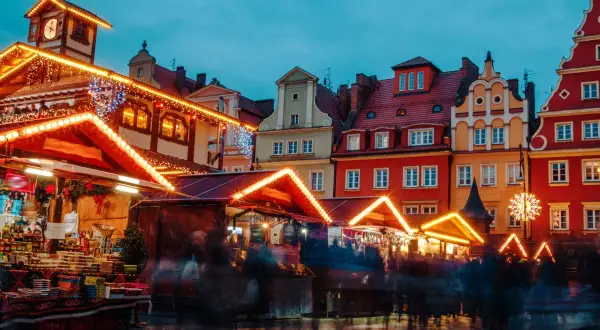 Bunte Häuser und beleuchtete Stände auf dem Wroclaw Weihnachtsmarkt. Menschen schlendern durch die festliche Atmosphäre.