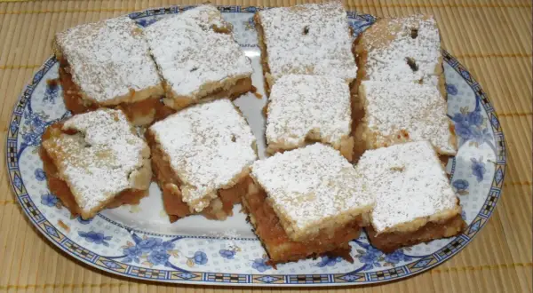 Na talerzu ułożono porcję 10 najlepszych ciast z jabłkami, posypanych cukrem pudrem.