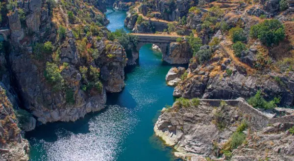 Cañón con río azul y puente de piedra, evocando la belleza natural de los pueblos de Madrid.