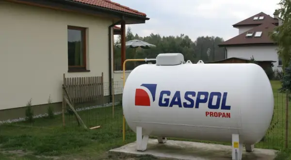 Duży, biały zbiornik z napisem GASPOL PROPAN, stojący obok domu. To jest propan, paliwo do ogrzewania.