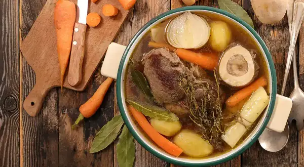 Un bol fumant de pot-au-feu, avec viande, carottes, pommes de terre, oignon et os à moelle. Une recette réconfortante.