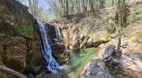 Cascata nella riserva naturale Alto Merse, con rocce colorate e acqua cristallina che forma una pozza verde smeraldo.