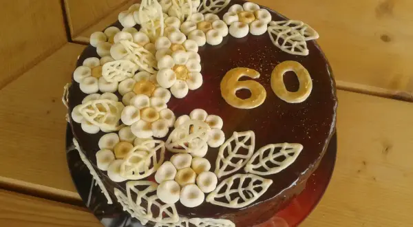 Elegancki tort na 60 urodziny dla mamy, ozdobiony czekoladowymi kwiatami i złotymi cyframi.