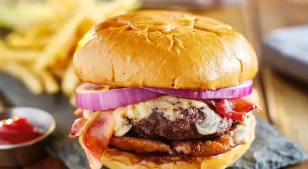 Soczysty burger z bekonem, serem i czerwoną cebulą, podany z frytkami i ketchupem.