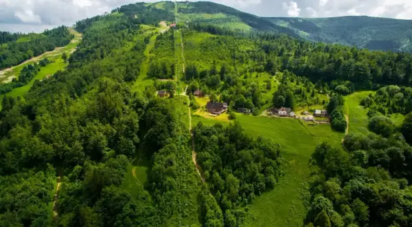 Widok z lotu ptaka na zielone zbocza Skrzycznego, z widocznymi trasami narciarskimi i szlakami pieszymi, domkami i kolejką linową.