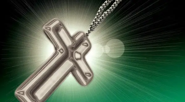 Srebrny krzyż na łańcuszku, otoczony blaskiem. Symbol nadziei i modlitwy za ojca.