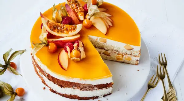 Eine köstliche Maracuja Torte mit frischen Früchten und Sahne. Ein Stück ist bereits angeschnitten, daneben liegen goldene Gabeln.