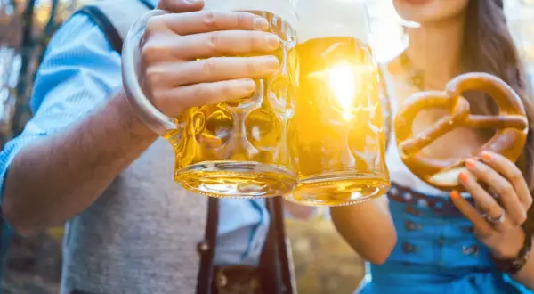 Zwei Hände halten Bierkrüge, ein Brezel wird gehalten. Die Sonne scheint, wie viel Prozent hat Oktoberfestbier?
