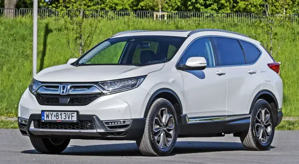 Biała Honda CR-V zaparkowana na zewnątrz, z zielenią w tle.
